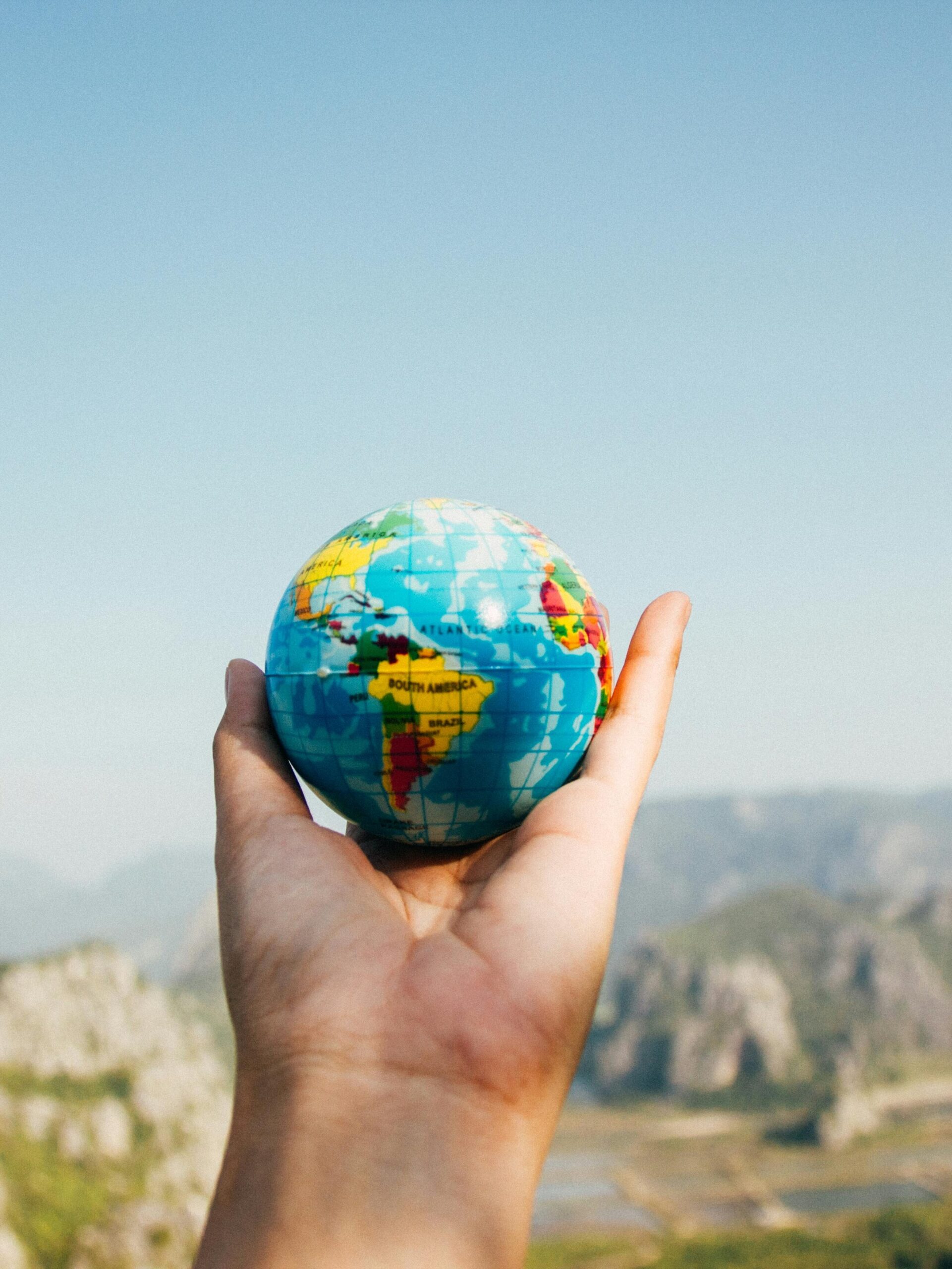 Hand holding a globe against a mountain background symbolizing travel and exploration.